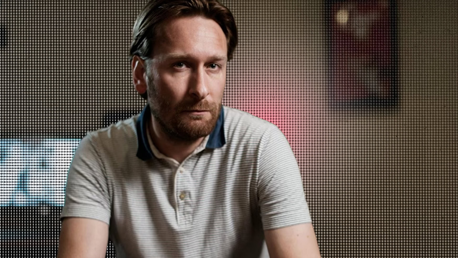 Man with beard and short hair in editing room, focused on screen.