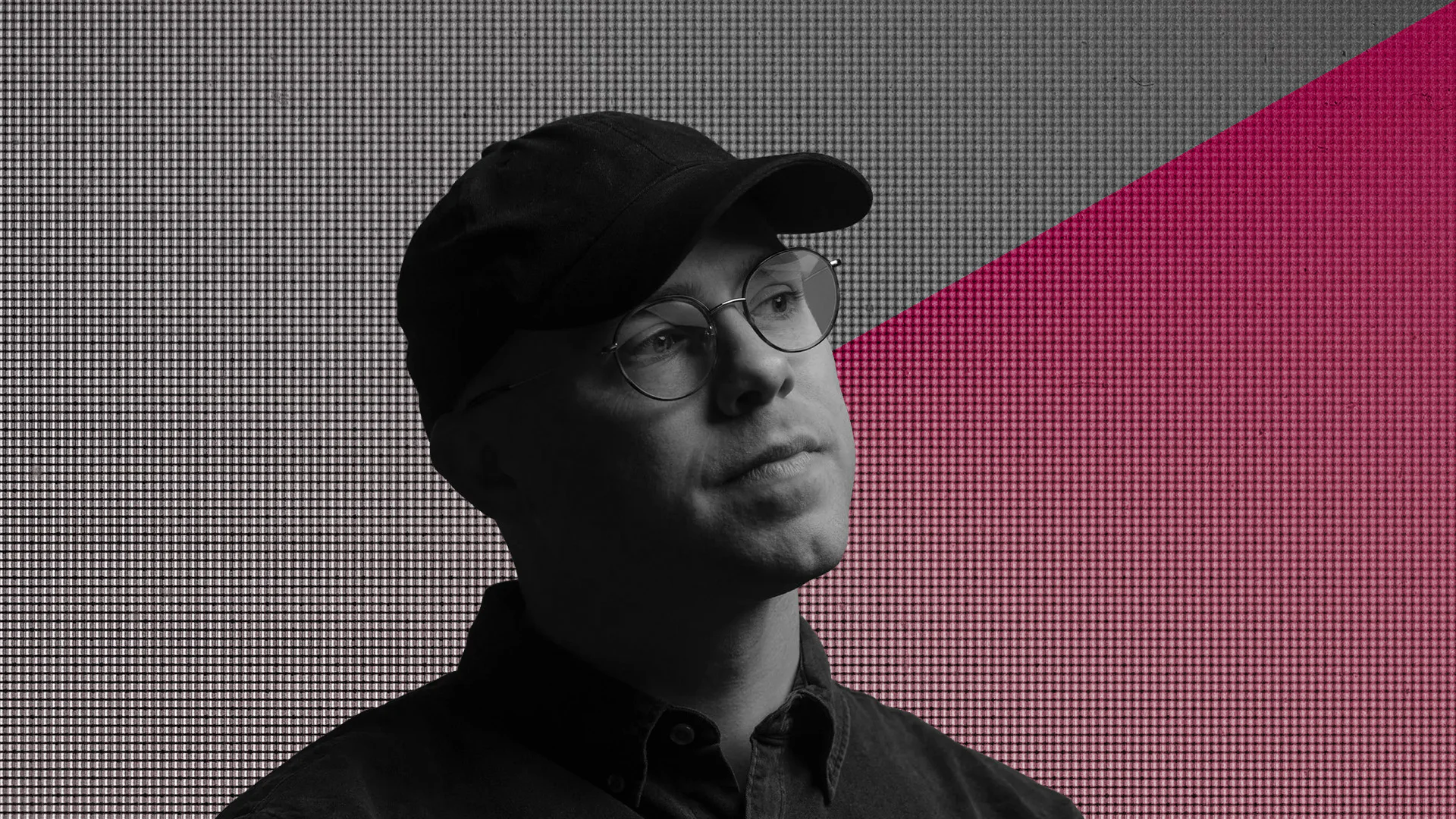 Young man wearing glasses and a cap, looking thoughtfully into the distance.