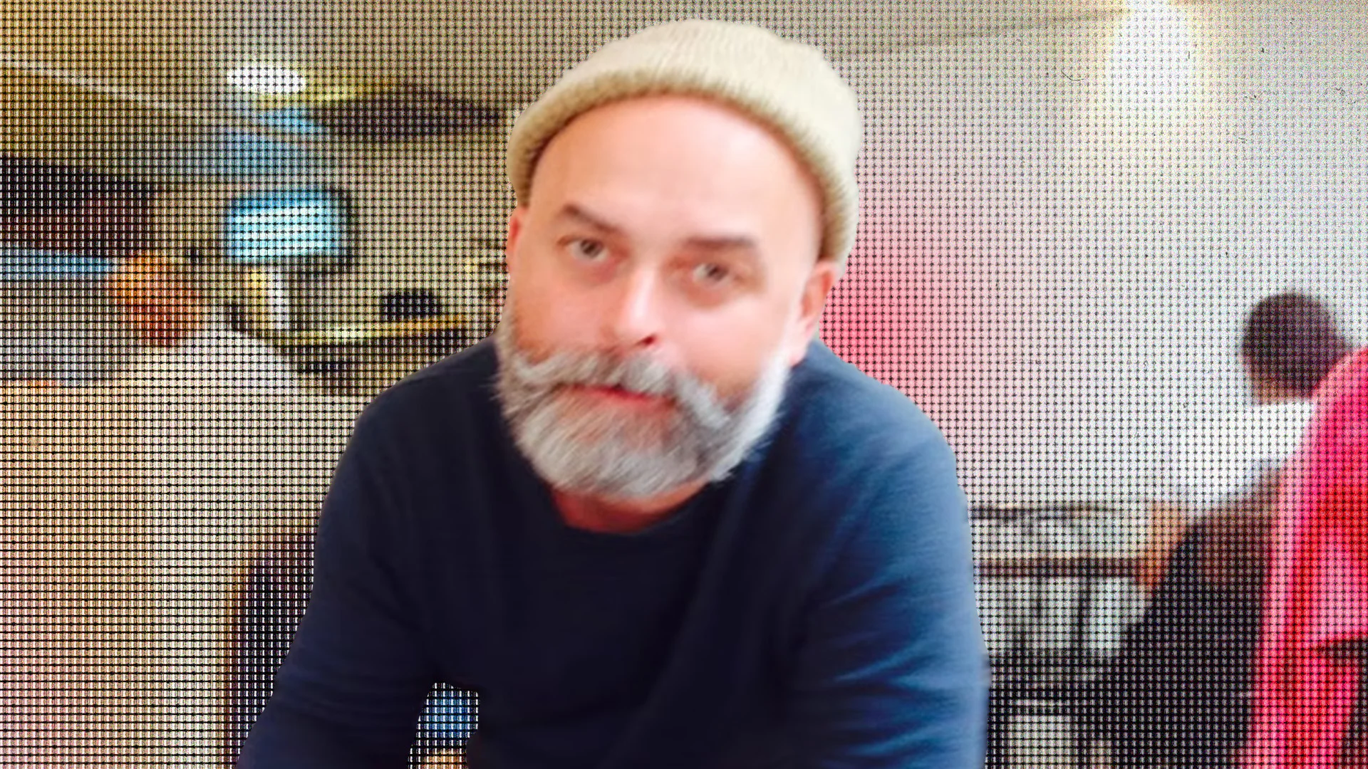 Man with a beard and beige hat in a busy indoor setting.
