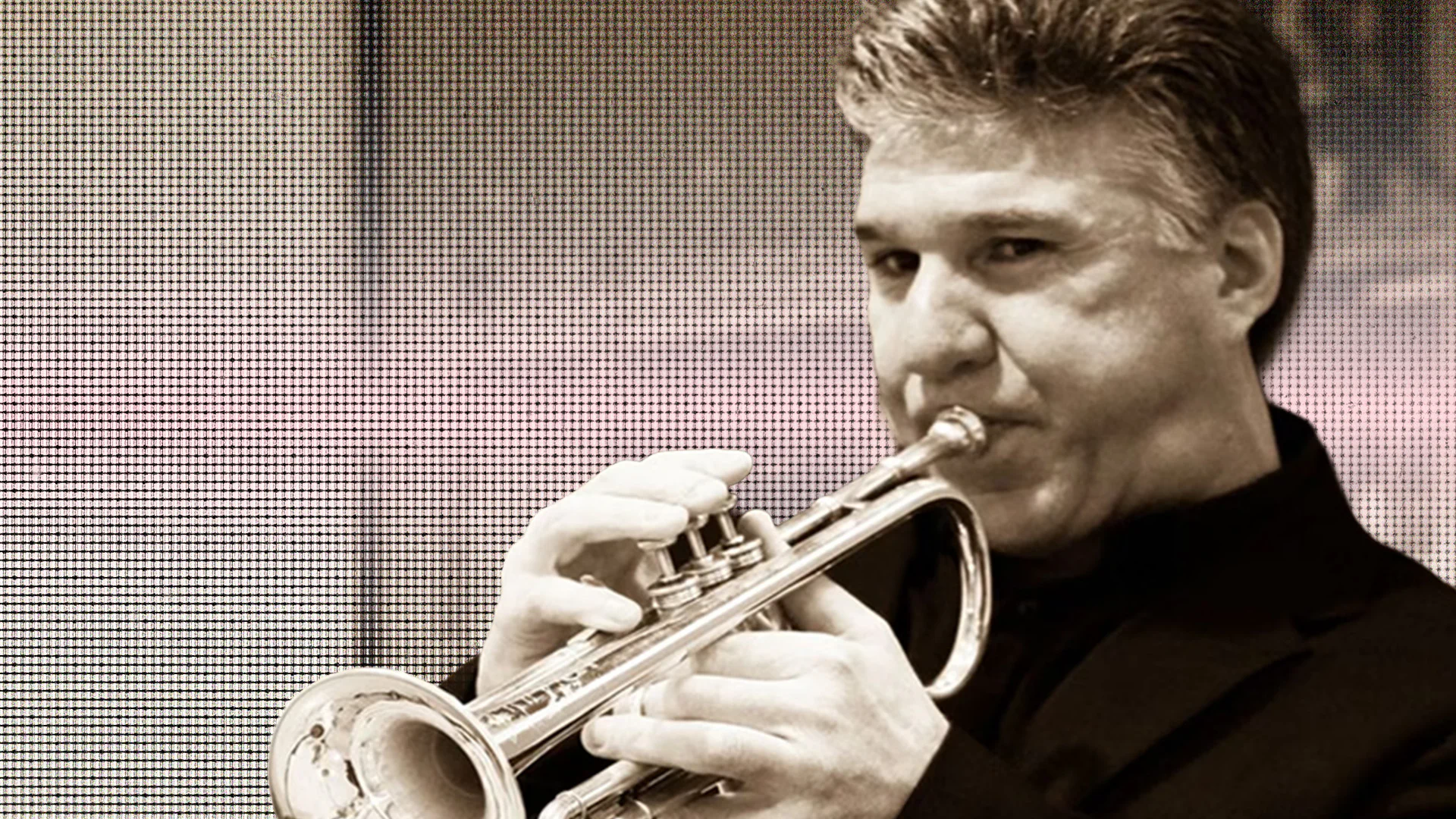 Male jazz musician playing trumpet in a black suit.