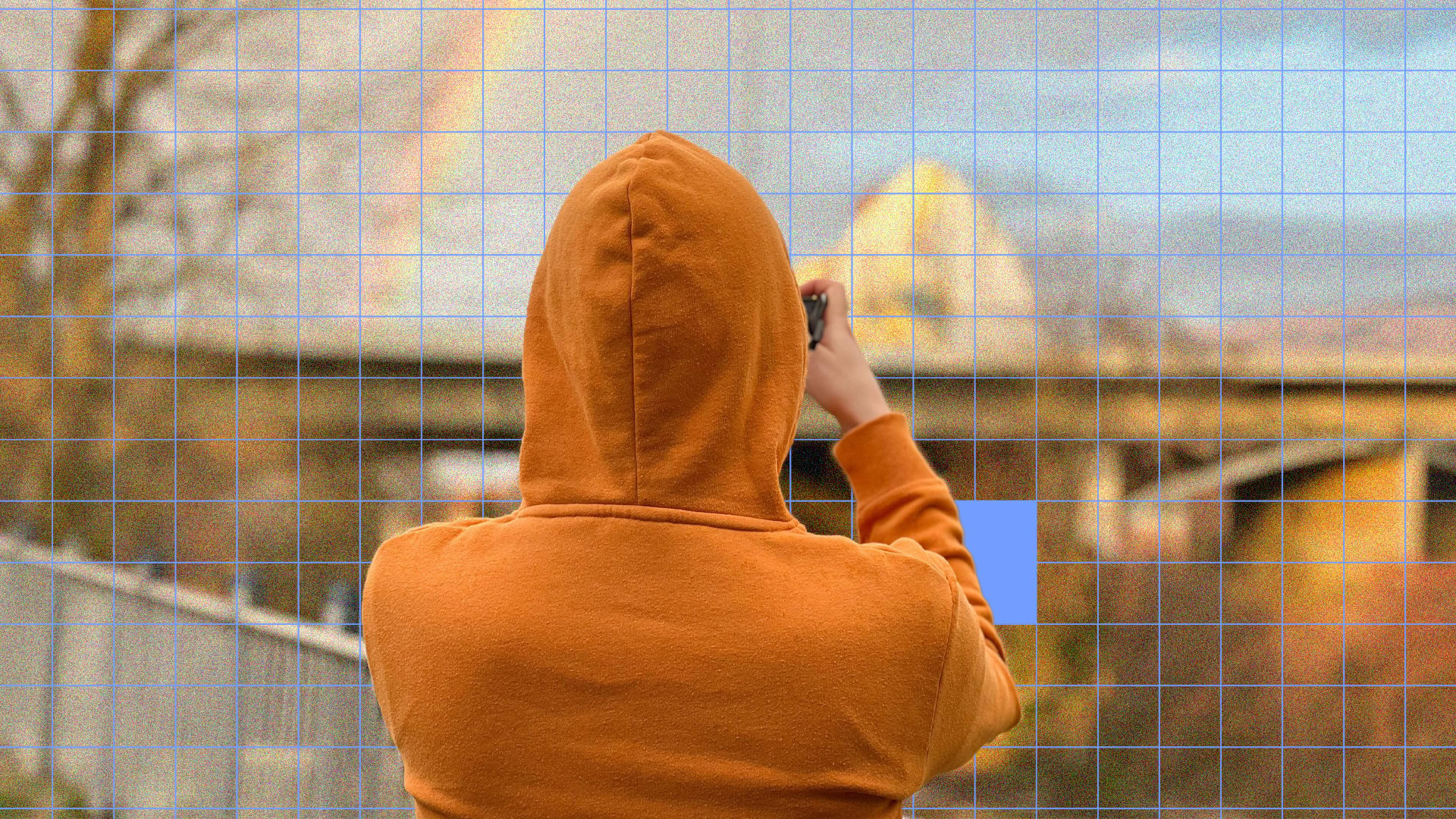 Person in orange hoodie capturing a landscape photo with smartphone.