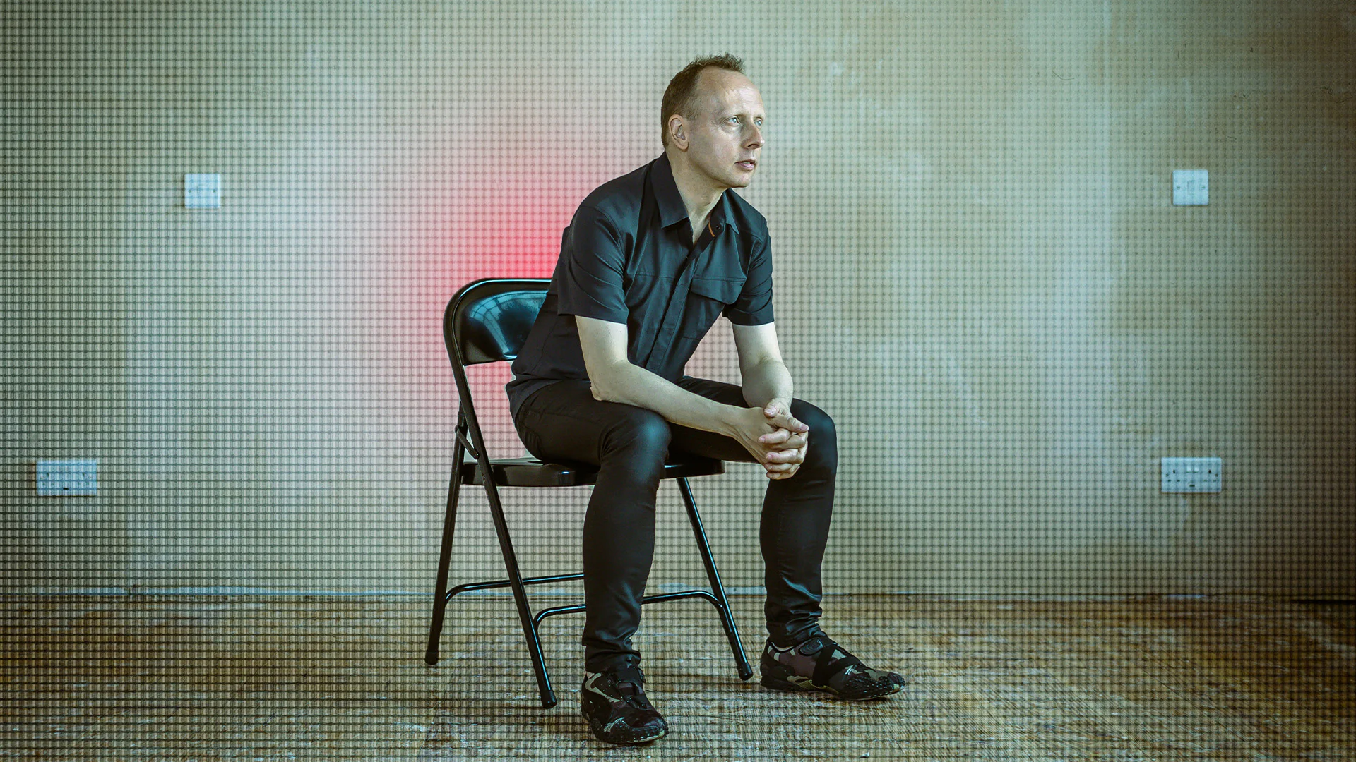 Man sitting on chair in a sound studio with LED lights and sound equipment.