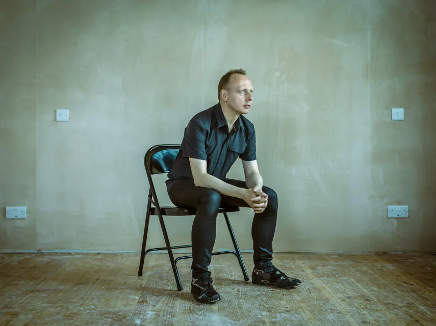 The artist, Scanner, sitting on a chair in an empty room