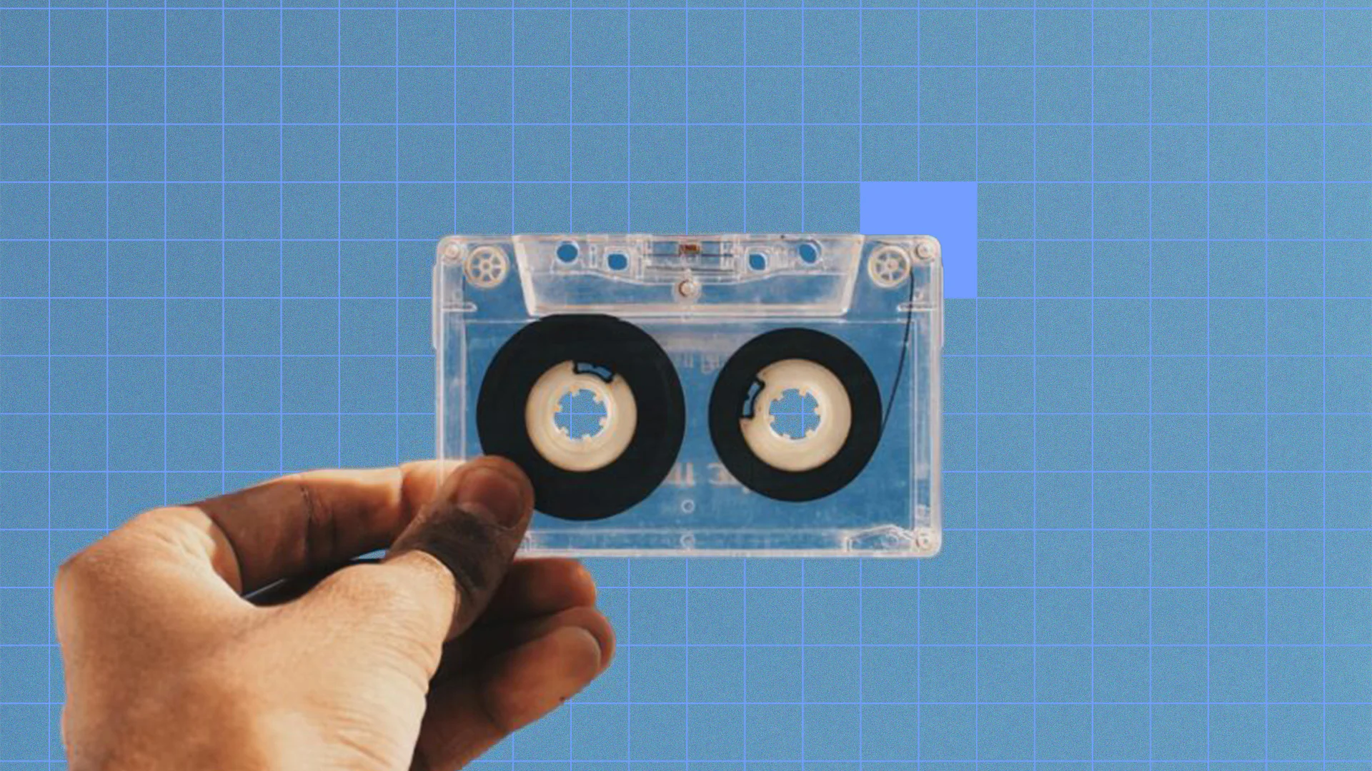 Clear cassette tape with black reels on blue grid background.