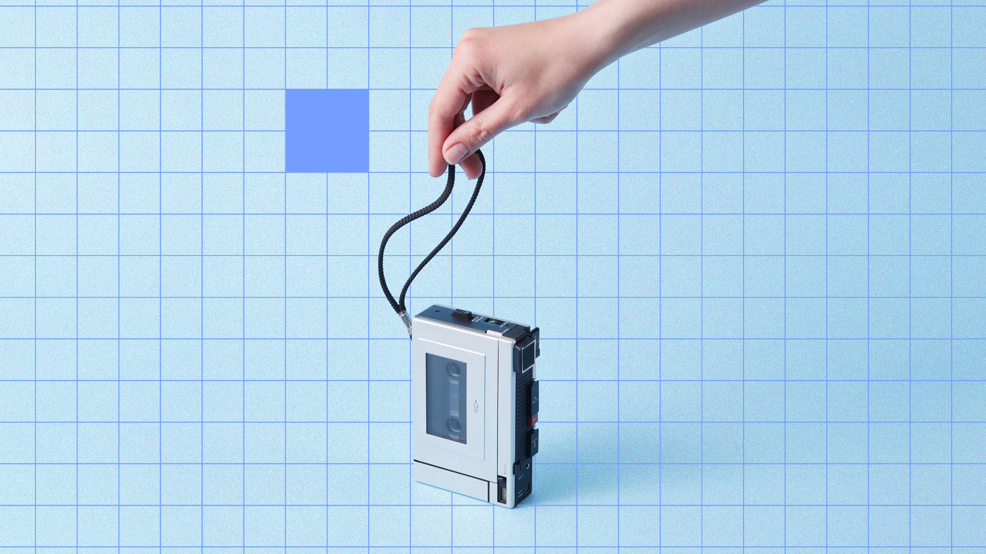 Hand holding a vintage Walkman against a blue grid background.